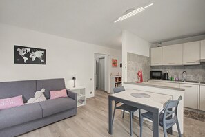 Un appartamento moderno con un divano grigio, un tavolo da pranzo con sedie, una cucina con mobili bianchi e una mappa del mondo appesa al muro.