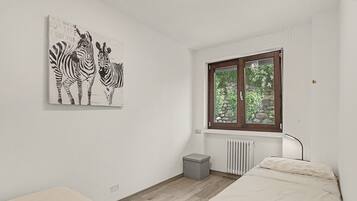 Quarto com duas camas, janela com vista para área verde, radiador e uma obra de arte com tema de zebra na parede.