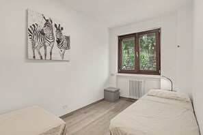 Camera da letto con due letti, una finestra vista sul verde, un termosifone e un'opera d'arte a tema zebra al muro.