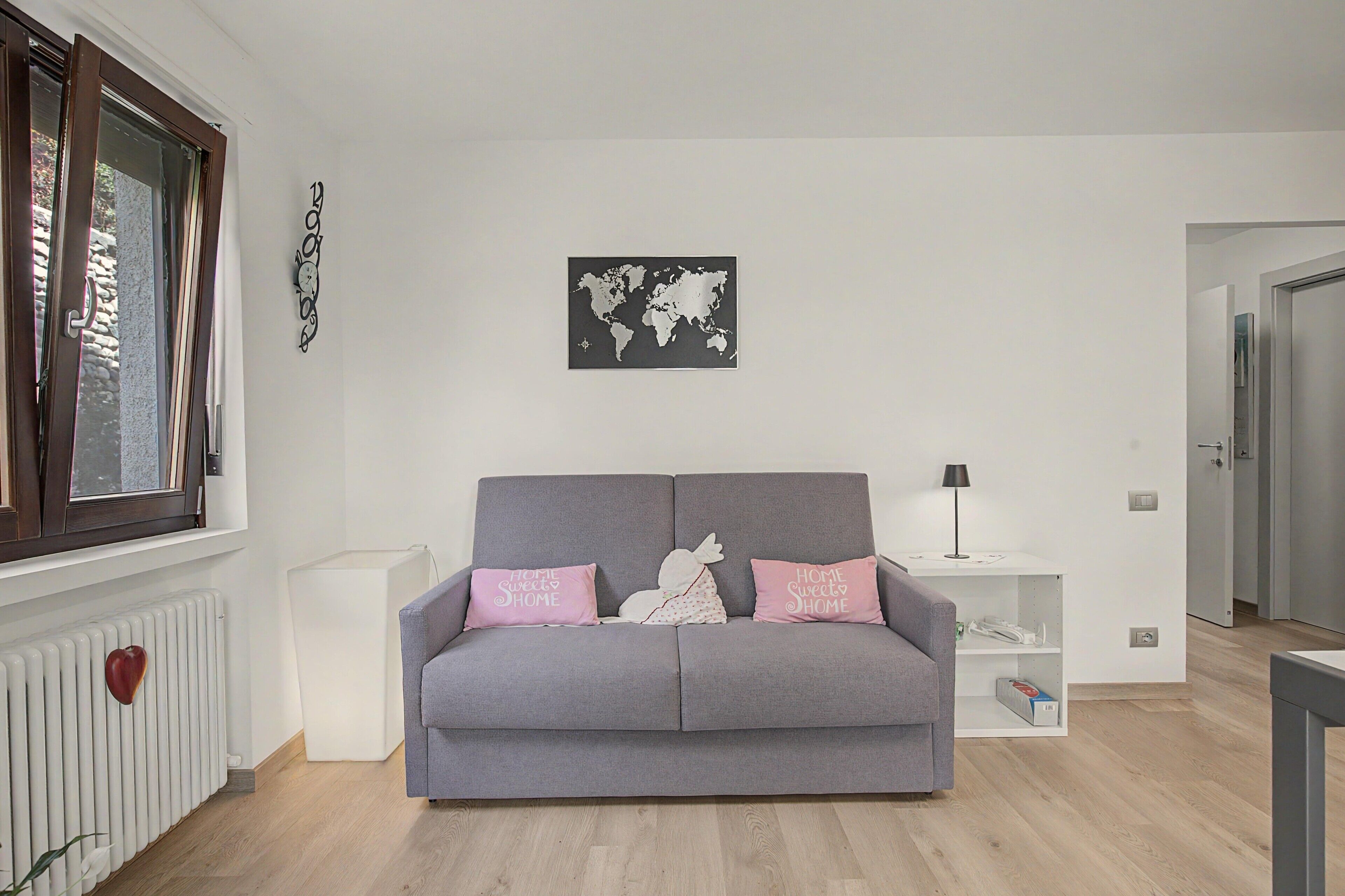 Um sofá cinzento com duas almofadas cor-de-rosa, um mapa-múndi na parede e um radiador branco.