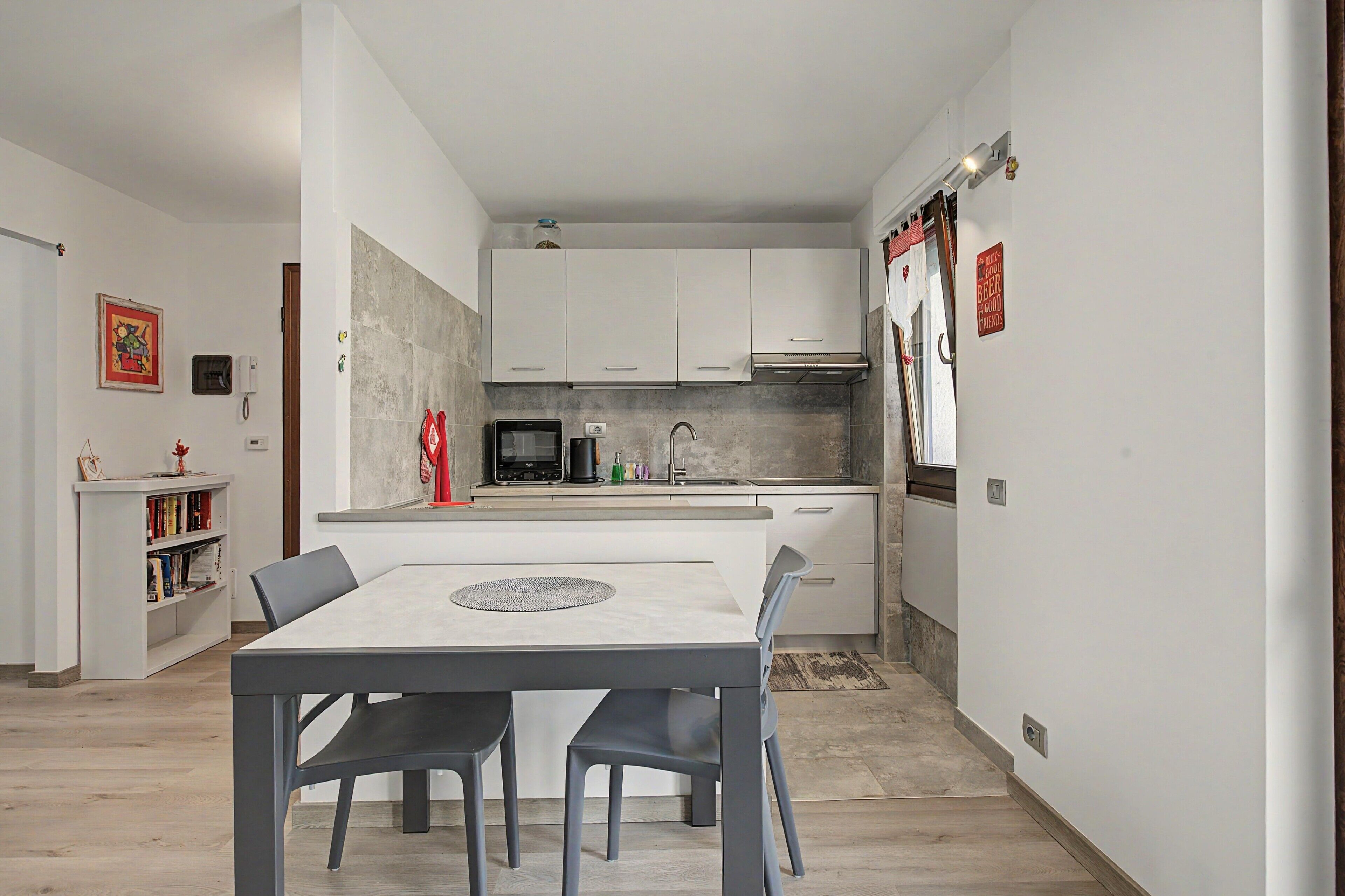 Una cocina compacta con armarios blancos, microondas y cafetera. Se observa una mesa de comedor con sillas al frente.