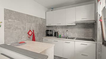 Cozinha moderna com armários brancos, pia de aço inoxidável e micro-ondas.