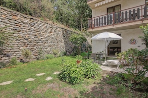 Un mur de pierre, un jardin avec une table et des chaises, et un bâtiment doté d’un balcon.