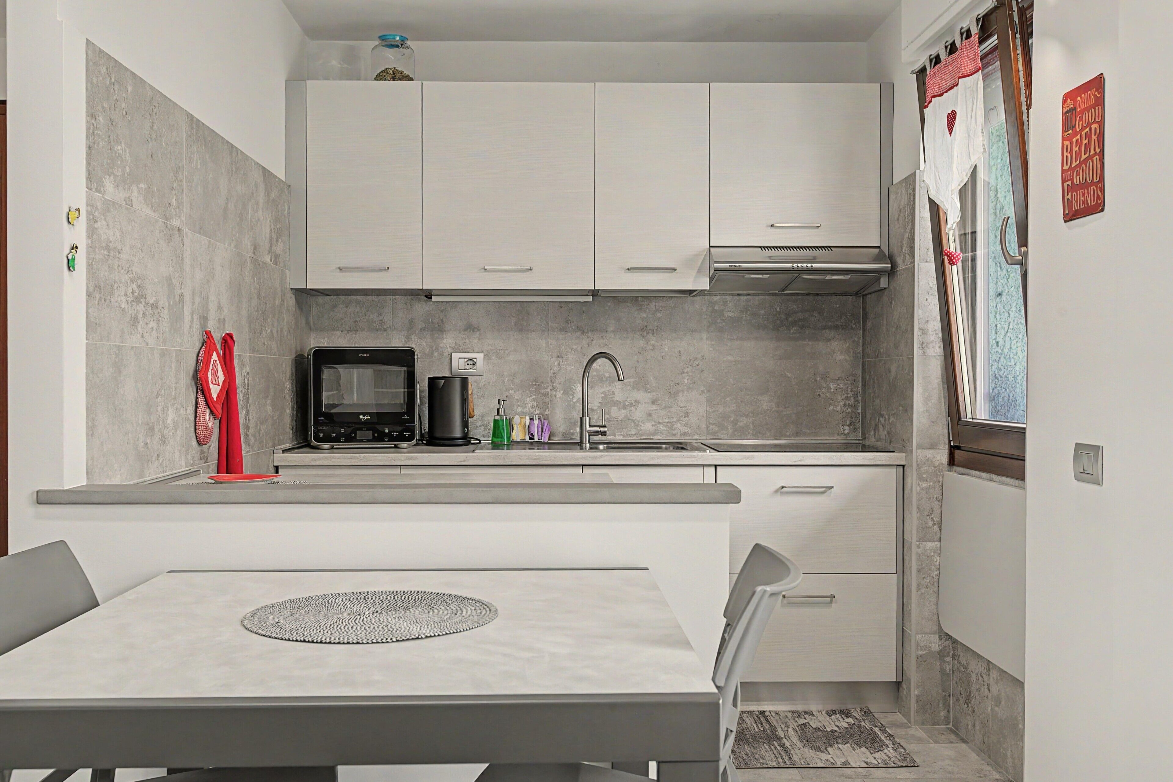 Una cocina moderna con armarios blancos, microondas, cafetera y lavamanos.
