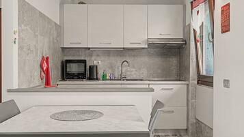 Una cocina moderna con armarios blancos, microondas, cafetera y lavamanos.