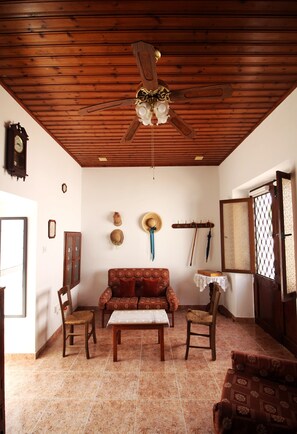 Une pièce avec un plafond en bois, un ventilateur de plafond, un canapé, deux fauteuils, une petite table et une porte avec une fenêtre.
