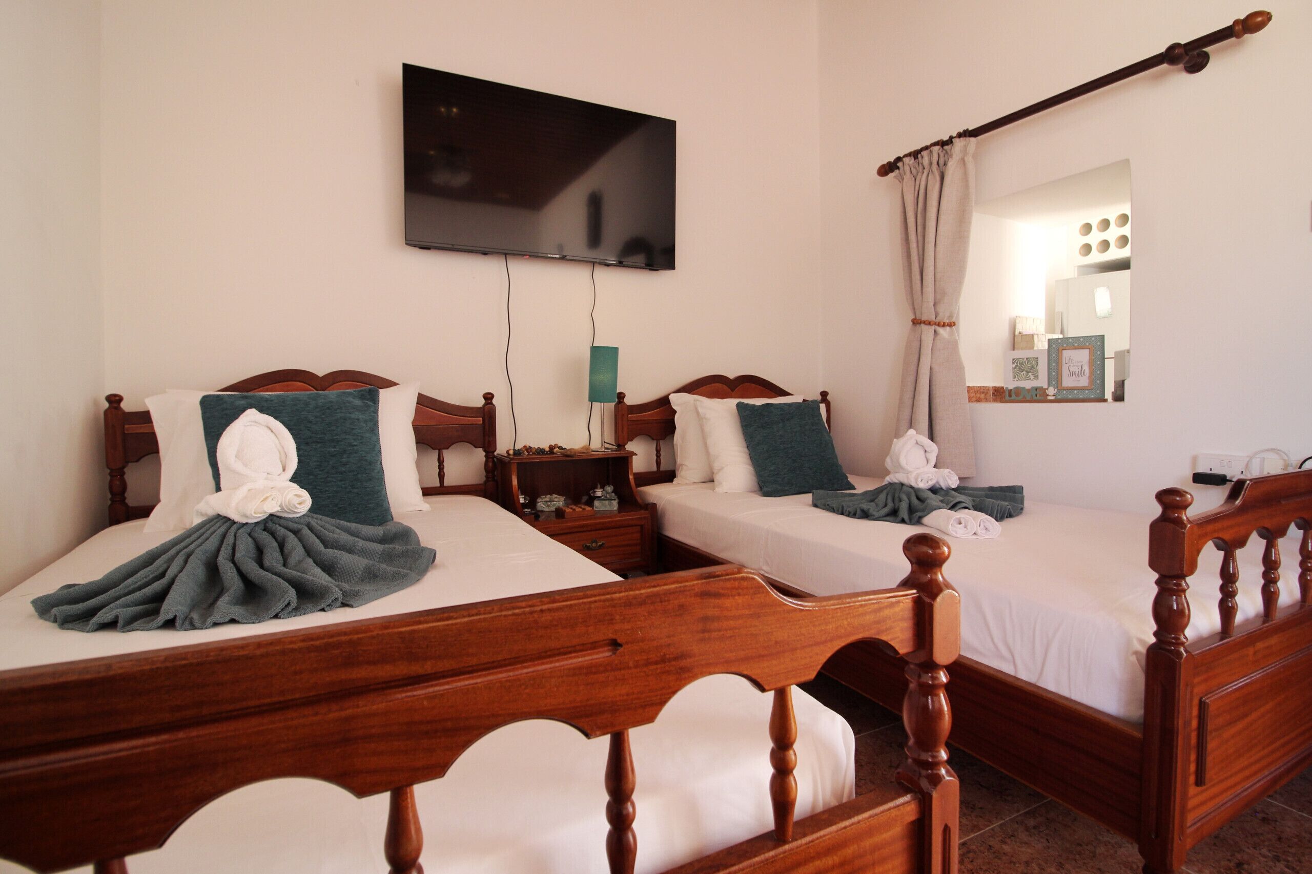 Una habitación de hotel con dos camas de madera, un televisor montado en la pared y una mesita de noche con una lámpara.