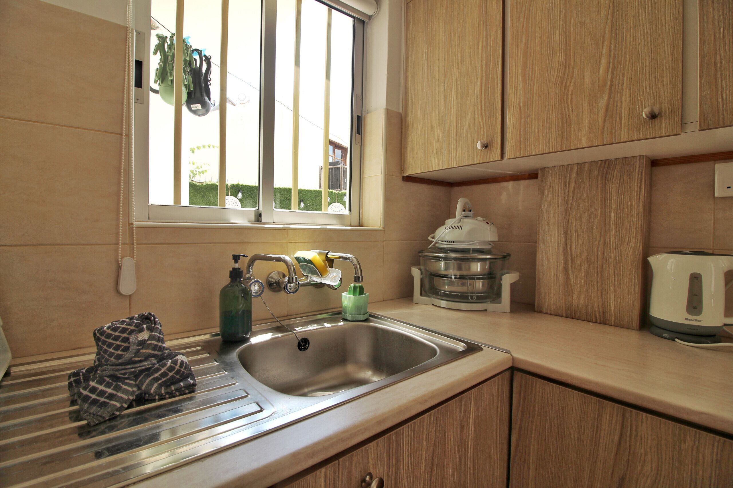 A kitchen with a stainless steel sink, a kettle, and a dish soap dispenser.