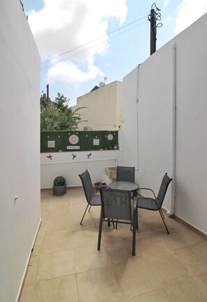 Une petite terrasse extérieure avec une table et des chaises, un pot de fleurs et un mur décoratif agrémenté d’une enseigne.