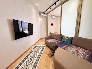 A modern living room with a flat-screen TV mounted on the wall, a sofa with patterned cushions, and a decorative rug. - STAY Prime View Apartment (Paralimni)