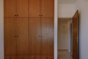 A wooden wardrobe with multiple compartments and a door leading to a hallway. - STAY Sunshine City Apartment (Larnaca)
