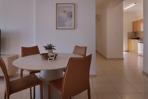 A dining area with a round table, four chairs, a small plant, and a framed picture on the wall. - STAY Sunshine City Apartment (Larnaca)