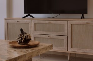 A wooden cabinet with a television on top, a decorative object on a table, and a tiled floor. - STAY Sunshine City Apartment (Larnaca)