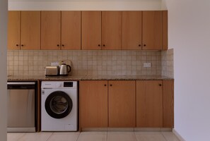 A kitchen with wooden cabinets, a washing machine, a toaster, and a kettle. - STAY Sunshine City Apartment (Larnaca)