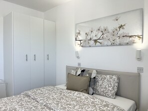 A bedroom with a bed, a wardrobe, and a wall-mounted artwork. - STAY Napa Zotiko Apartment (Ayia Napa)