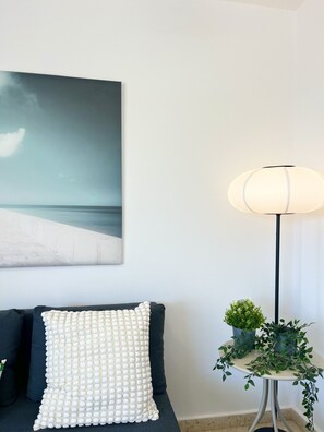 A room with a sofa, a lamp, a small table with plants, and a wall-mounted painting. - STAY Napa Zotiko Apartment (Ayia Napa)