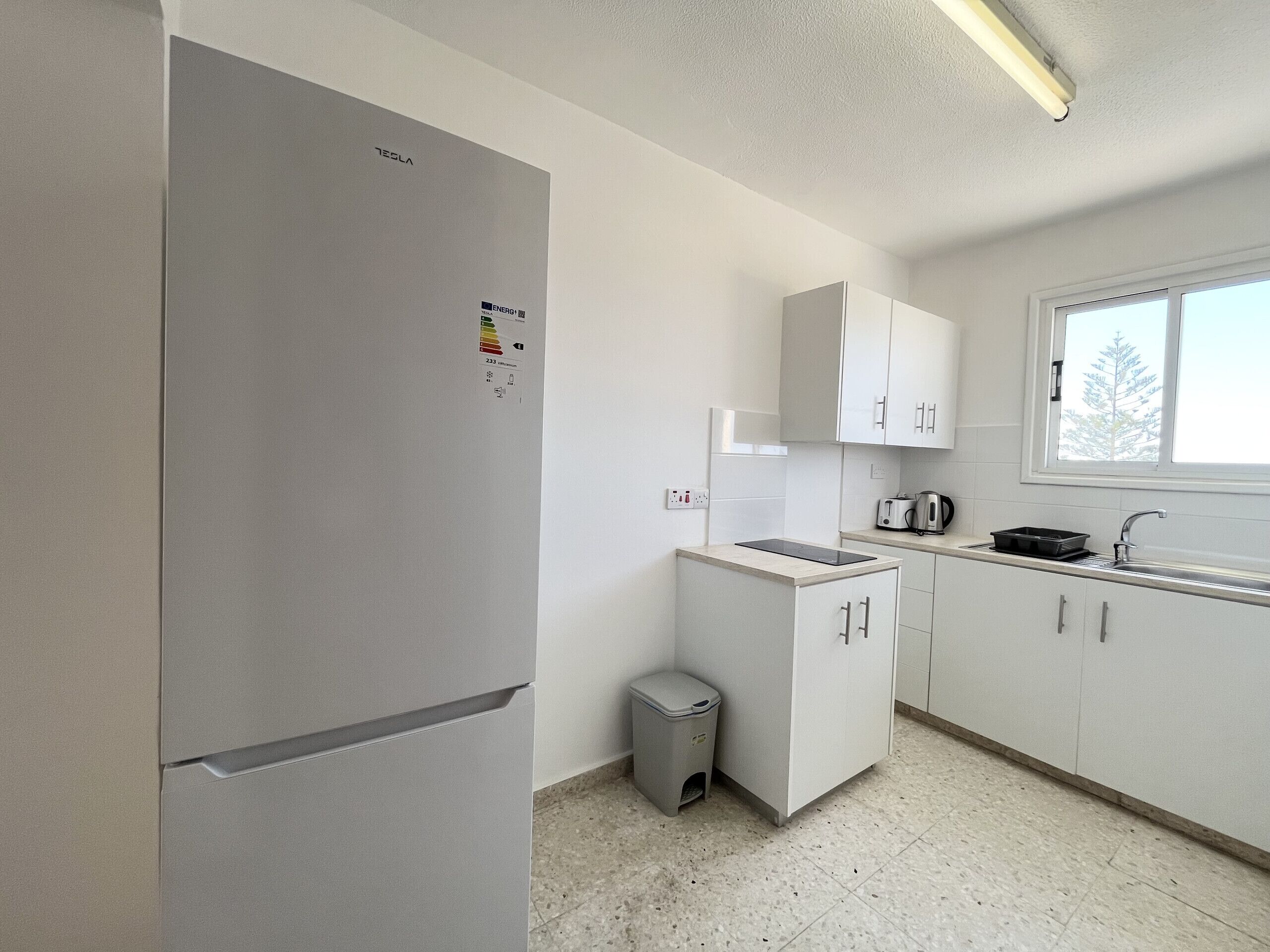 Una cocina moderna con refrigerador empotrado, un lavamanos pequeño y una ventana sobre la encimera.