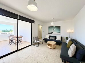 A modern living room with a glass door leading to a balcony, a sofa set, a coffee table, and a painting on the wall. - STAY Napa Zotiko Apartment (Ayia Napa)