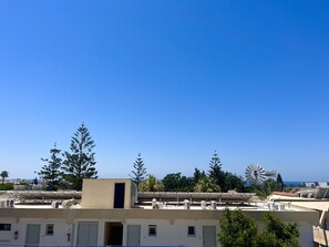 Eine Dachterrasse mit Solaranlagen, einer Windturbine und einem Gebäude mit einer beigefarbenen Fassade.