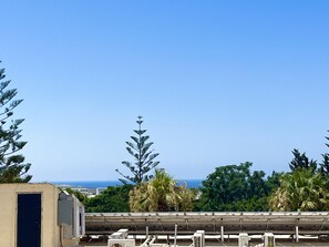 A rooftop with solar panels, a building with a closed shutter, and a view of the ocean. - STAY Napa Zotiko Apartment (Ayia Napa)