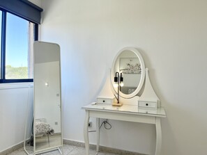 A room with a white vanity table, a round mirror, and a bed with a patterned bedspread. - STAY Napa Zotiko Apartment (Ayia Napa)