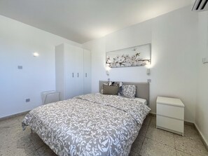 A bedroom with a bed, a wardrobe, a nightstand, and a wall-mounted light fixture. - STAY Napa Zotiko Apartment (Ayia Napa)
