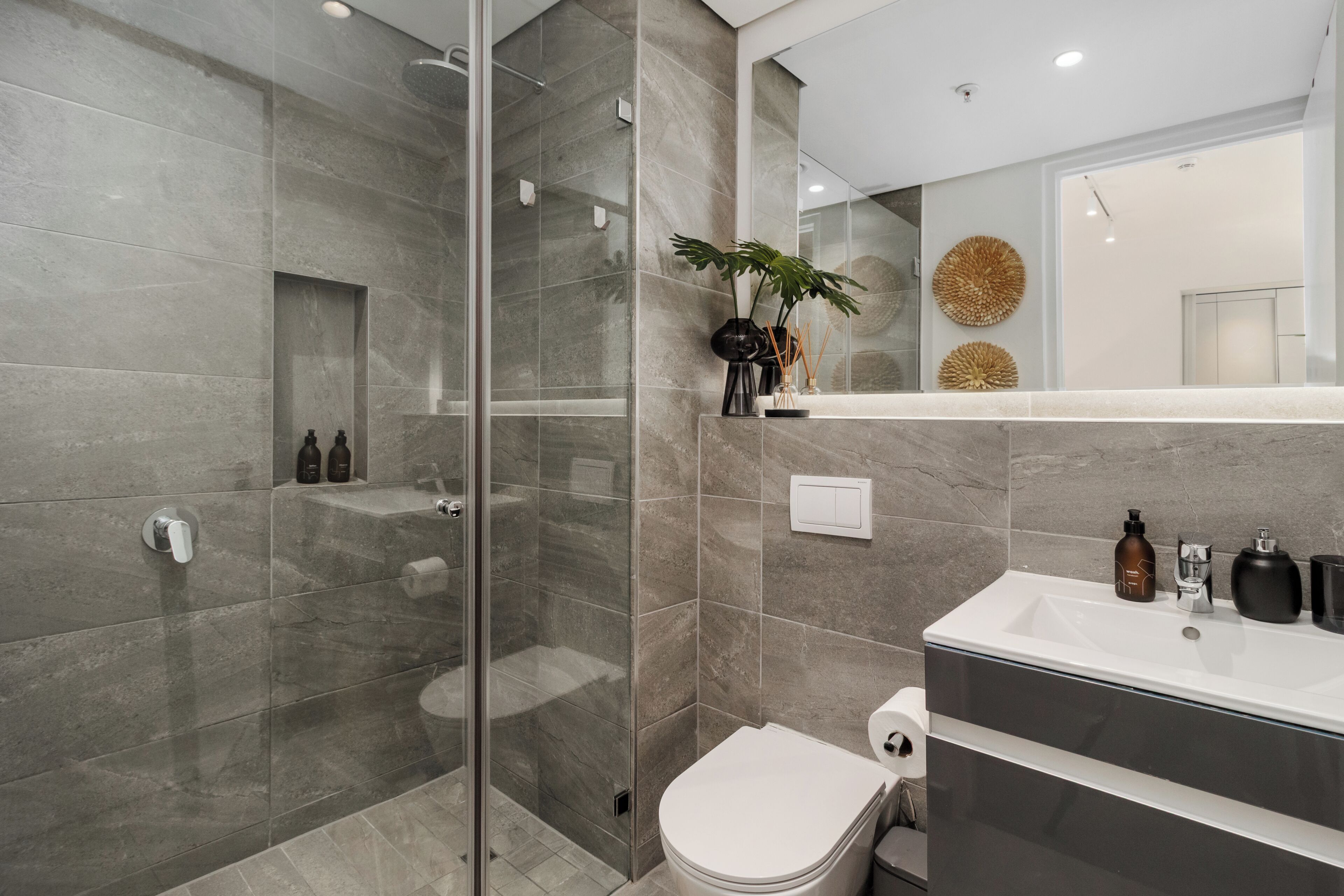 A modern bathroom with a glass-enclosed shower, a toilet, and a sink area with toiletries.
