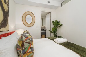 Ein Hotelzimmer mit einem Bett, einem runden Spiegel, einer Topfpflanze und Blick ins Badezimmer.