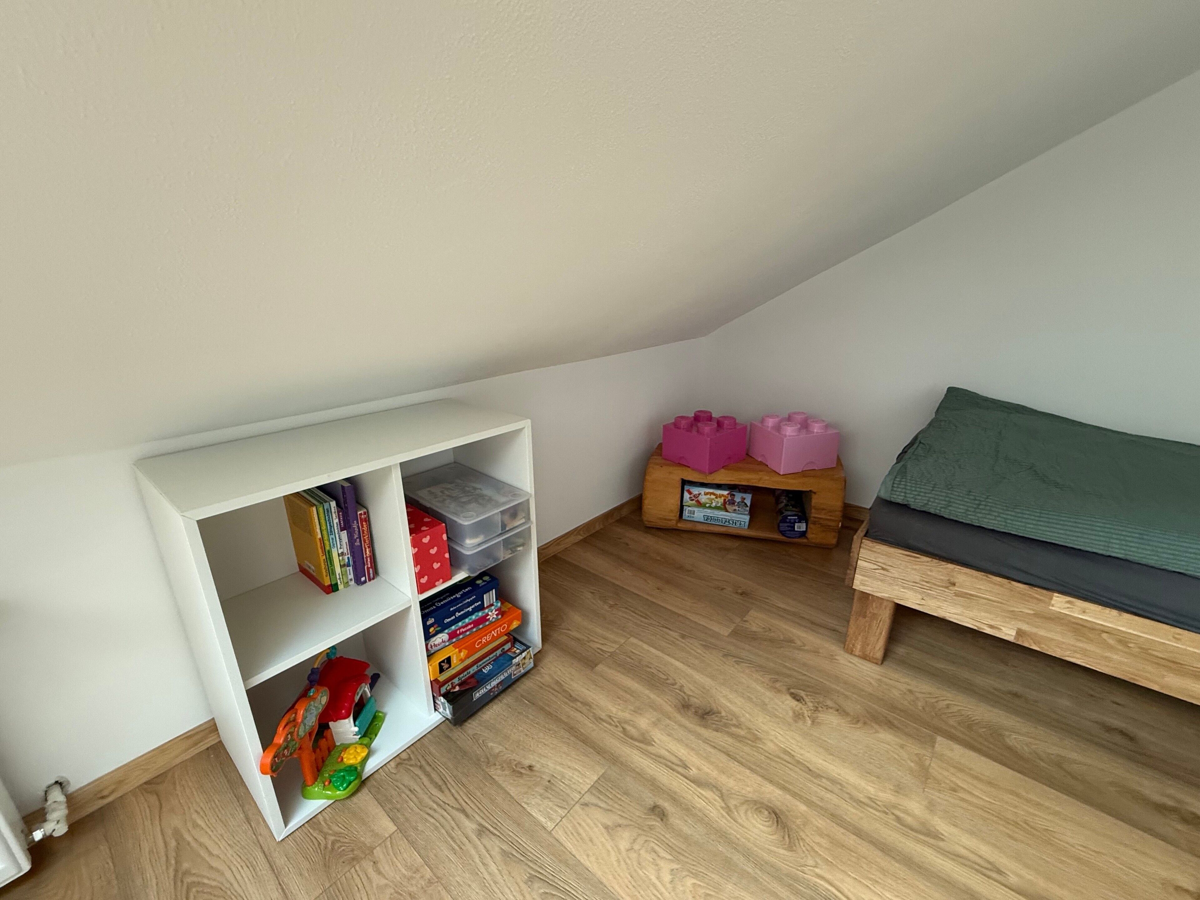 Een kamer met een witte boekenkast, een houten bankje en een klein tafeltje met speelgoed.