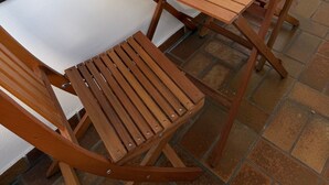 A wooden table and chairs set up on a patio with a view of a window.