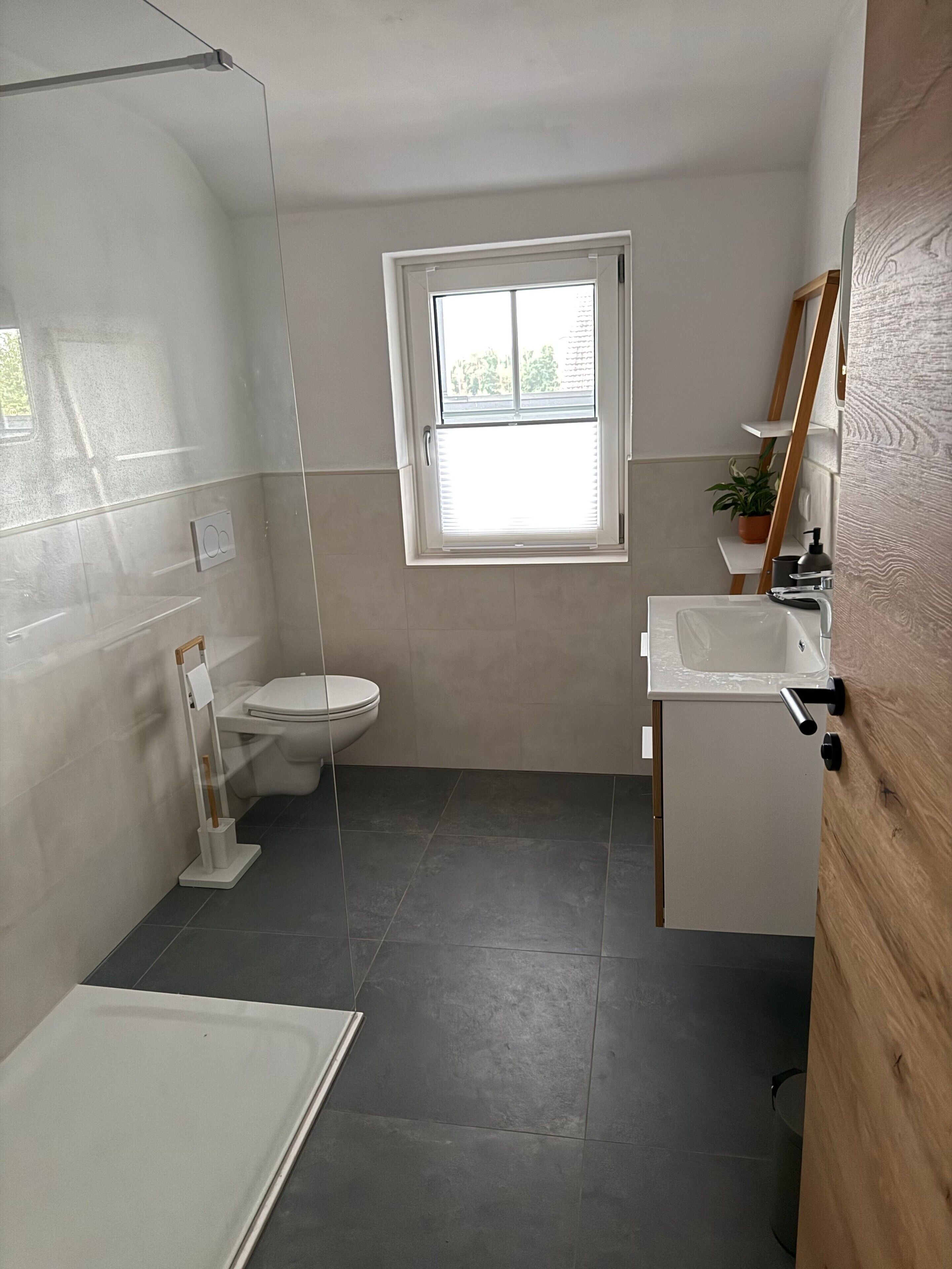 Ein Badezimmer mit Toilette, Waschbecken und Dusche. Über der Toilette befindet sich ein Fenster.