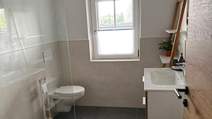 A bathroom with a toilet, sink, and shower. There is a window above the toilet.
