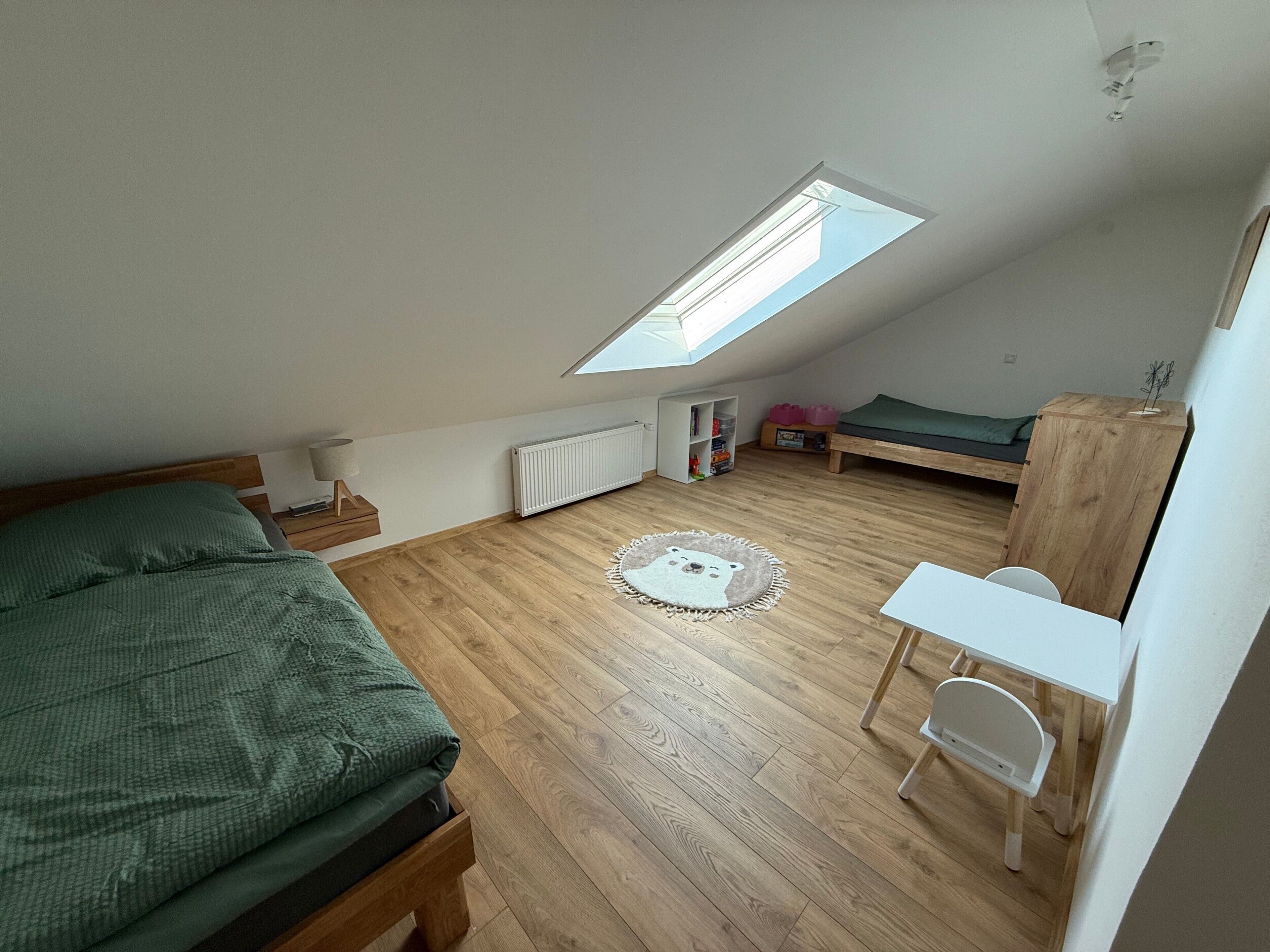 Ein kleiner, ordentlicher Raum mit schrägem Dach, einem Bett, einem Schreibtisch und einem Stuhl.