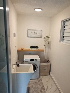 A laundry room with a washing machine, a drying rack, a shelf with a plant, and a wall-mounted sign. - 2-bedroom with JACUZZI and WATER BACKUP in charming Carolina (Carolina)