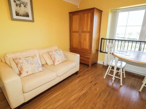 A living room with a beige sofa, wooden cabinet, and a dining table with chairs. - The Mummers Studio Apartment 1 (Enniskillen)