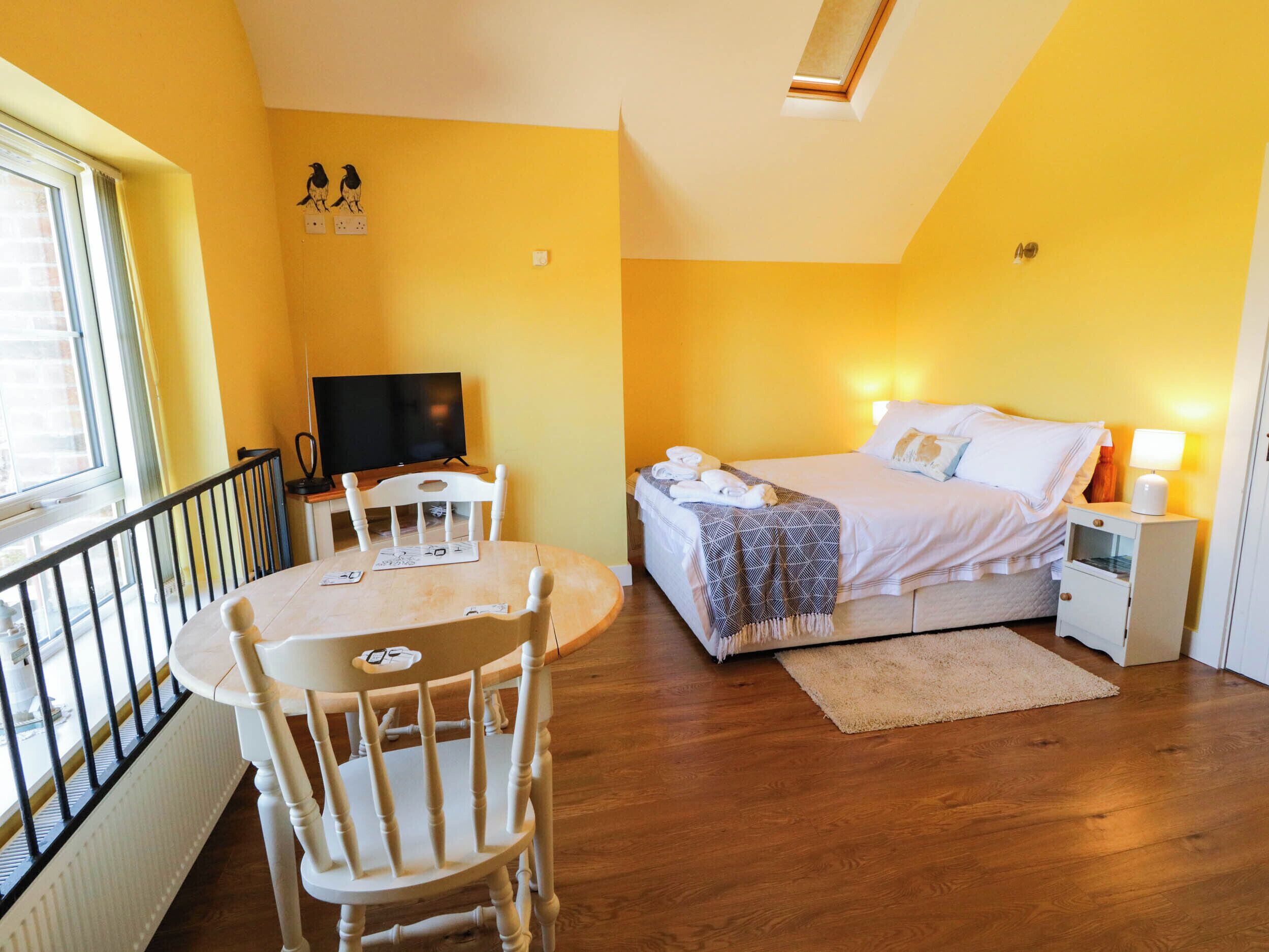 A room with a bed, a TV, a dining table with chairs, and a window.