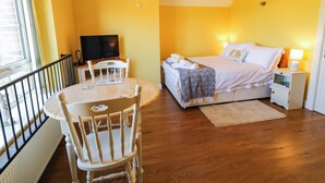 Quarto com cama, televisão, mesa de jantar com cadeiras e janela.