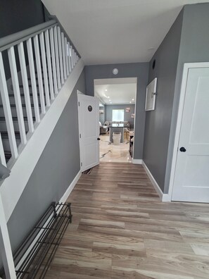 A hallway with a staircase, a door, and a view into a living area with a couch and a dining table. - Terrific 3-bedroom house with AC , one and a half bath in charming Zanesville oh (Zanesville)