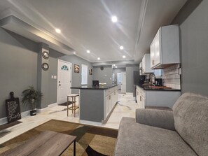 Une cuisine moderne avec des meubles gris, un îlot central et un coin repas comprenant un canapé et une table basse.