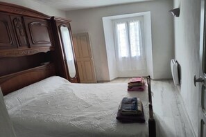 A bedroom with a wooden headboard, a bed with a white bedspread, a window with a view, and a door. - One-bedroom apartment in Venzolasca (Venzolasca)
