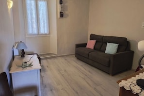 A living room with a sofa, a small table with a lamp, and a window with curtains. - One-bedroom apartment in Venzolasca (Venzolasca)