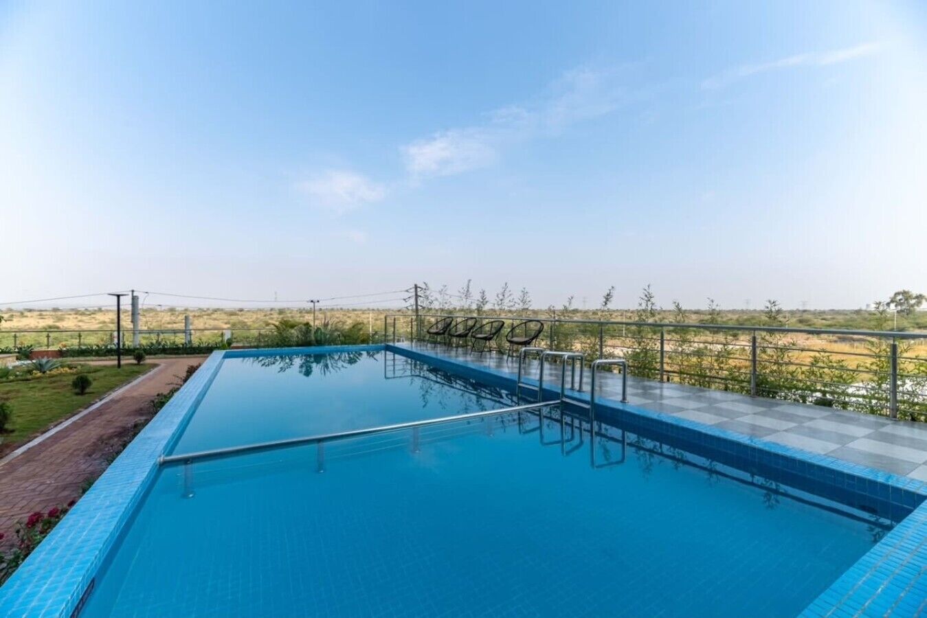 A rectangular swimming pool with a clear blue water surface, surrounded by a low metal fence, and a view of a flat landscape in the background.