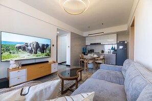 A modern living room with a flat-screen TV, a sofa, a dining area with chairs, and a kitchen in the background. - The Safari view Gateway | 10 Min JKIA | 5 Min SGR (Nairobi)