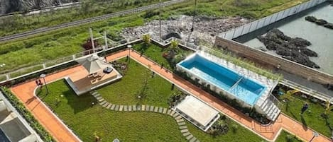 Zona ajardinada con piscina, senderos y un pequeño edificio.