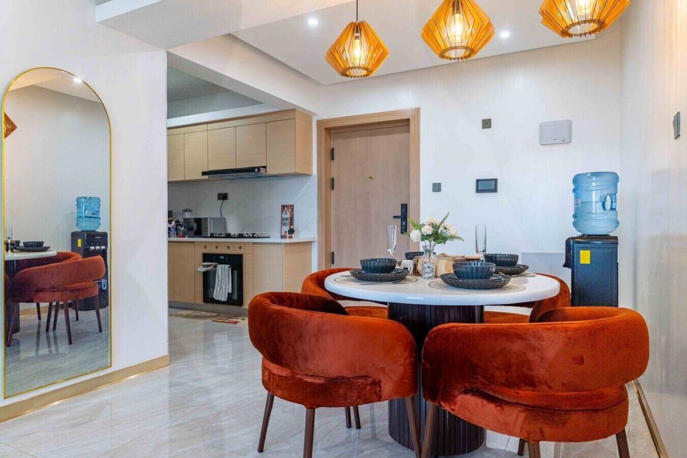 Een moderne eetruimte met een ronde tafel, rode fluweelstoelen en hanglampen.