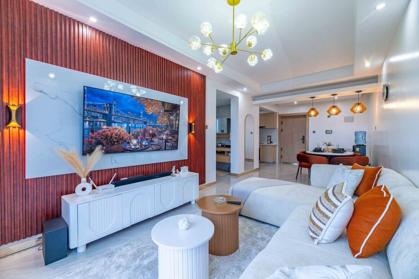A modern living room with a flat-screen TV, white sofa, and a dining area.