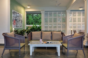 Un área de estar con mobiliario de mimbre y una mesa de centro blanca, rodeada por una celosía blanca decorativa.