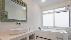 Un baño moderno con una bañera independiente grande, un lavabo blanco y un espejo amplio con marco decorativo.