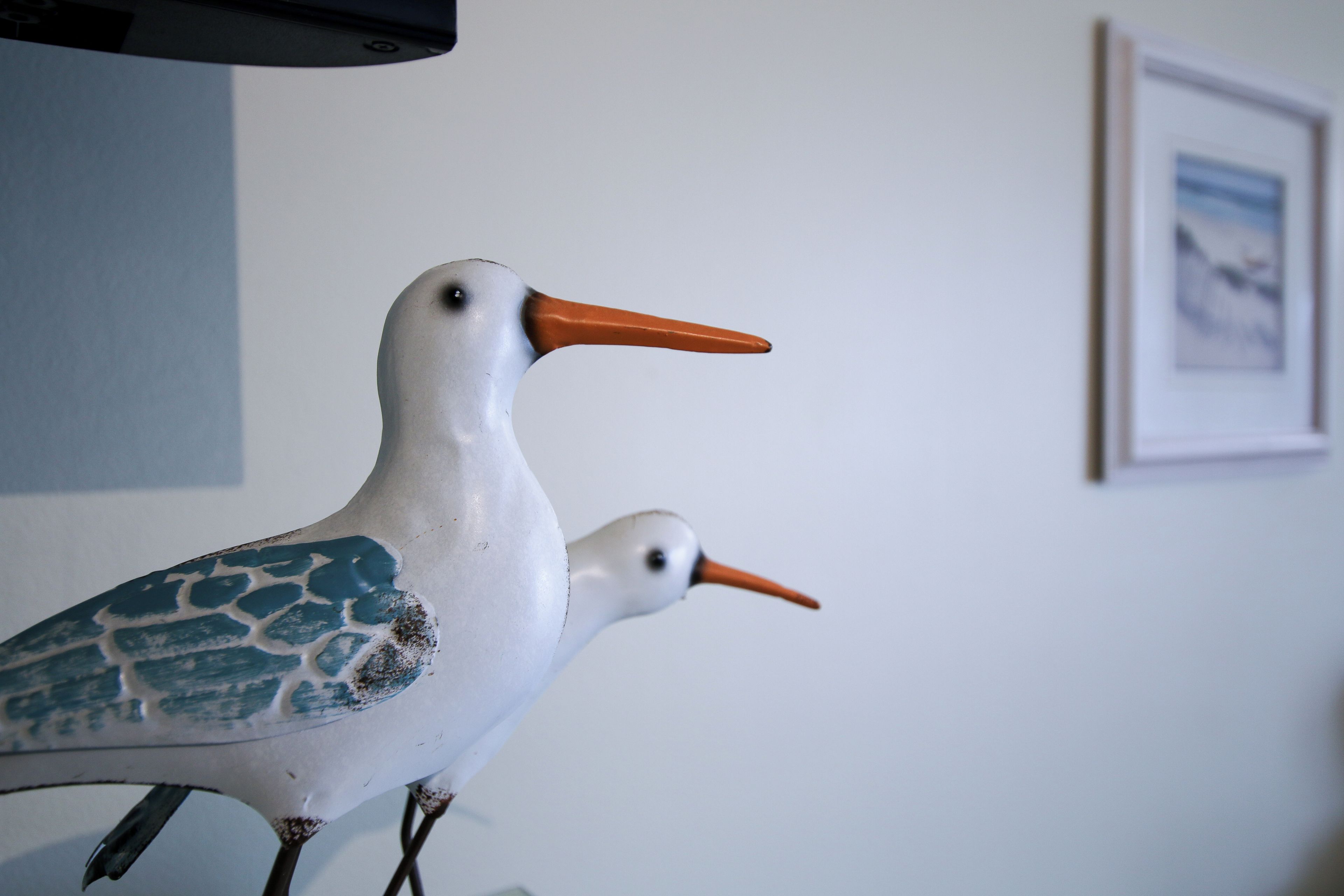 Duas figuras de pássaros em uma prateleira em frente a uma parede com um quadro emoldurado.
