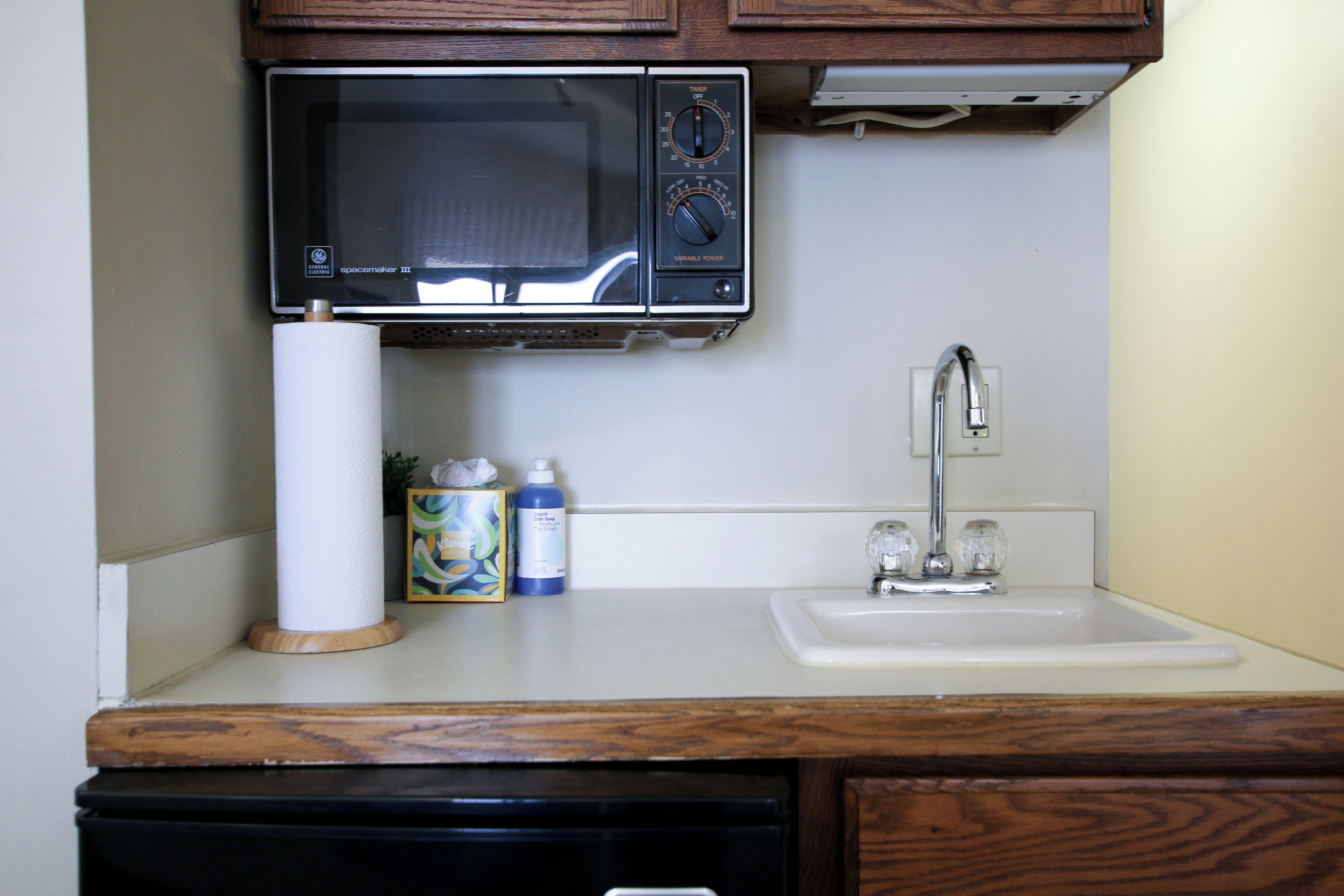 A kitchen with a microwave, a sink, and a dish soap bottle.